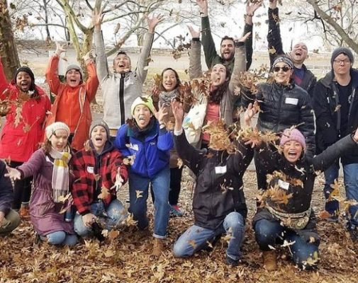 A group of volunteers throws leaves in the air for a photo op
